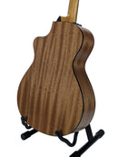 The back of a wooden acoustic guitar with a cutaway body, displayed on a black stand against a light gray background.