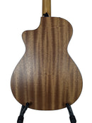 The back of a wooden acoustic-electric guitar, showcasing a rich brown wood grain finish, displayed on a black stand against a light gray background.