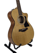 A Taylor acoustic guitar with a natural wood finish and black pickguard, displayed on a black stand against a light gray background.