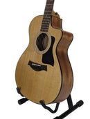 An acoustic-electric guitar with a natural wood top and dark brown sides, displayed on a black stand against a light gray background.