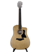 A 12-string acoustic-electric guitar with a natural wood finish and black pickguard, displayed on a stand against a neutral gray background.