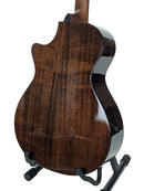 The back of a glossy dark brown wooden acoustic guitar, showing the rich grain pattern and high-gloss finish, displayed on a black stand against a white studio background.