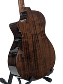 The back of a dark brown acoustic-electric guitar with a glossy finish, displayed on a black stand against a white background.