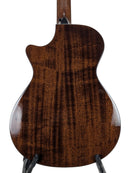 The back of a wooden acoustic guitar with a glossy, figured maple top, displayed on a black stand against a white background.