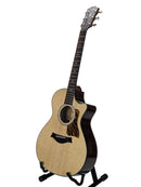 An acoustic-electric guitar with a natural wood top and dark body, displayed on a black stand against a light gray background.