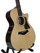 An acoustic-electric guitar with a natural wood top, dark brown sides, and a cutaway body, displayed on a black stand against a light gray background.