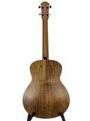 The back of an acoustic guitar with a natural wood finish, displayed on a stand against a light gray background.