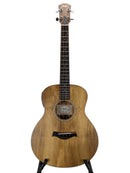 A Taylor acoustic guitar with a natural wood finish, displayed on a black stand against a light gray background.