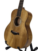 A natural wood acoustic guitar with a cutaway body, displayed on a black stand against a light gray background.