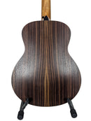 The back of a wooden acoustic guitar, showing a dark brown wood grain finish, displayed on a black stand against a white background.