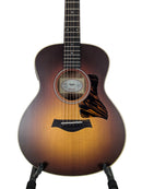 Taylor acoustic guitar with a classic sunburst finish, resting on a black guitar stand against a light gray background.