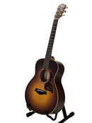A 12-string acoustic guitar with a natural sunburst finish, displayed on a black stand against a light gray background.