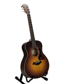 A Taylor acoustic-electric guitar in a sunburst finish, displayed on a black stand against a light gray studio background.
