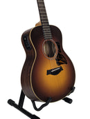 Taylor acoustic-electric guitar with a sunburst finish, shown on a black stand against a white studio background.