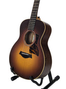 A Taylor acoustic guitar with a sunburst finish, displayed on a black stand against a light gray background.